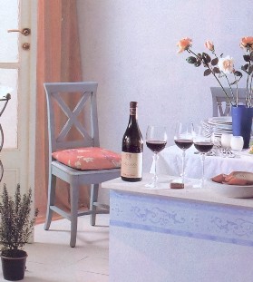 In einer Küche: Wein auf der Anrichte, ein Kissen auf einem Stuhl, ein Vorhang am Fenster – und Tapeten geben dem Raum sein besonderes Flair.