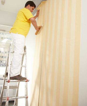 Ein Maler steht beim Tapezieren auf einer Leiter.